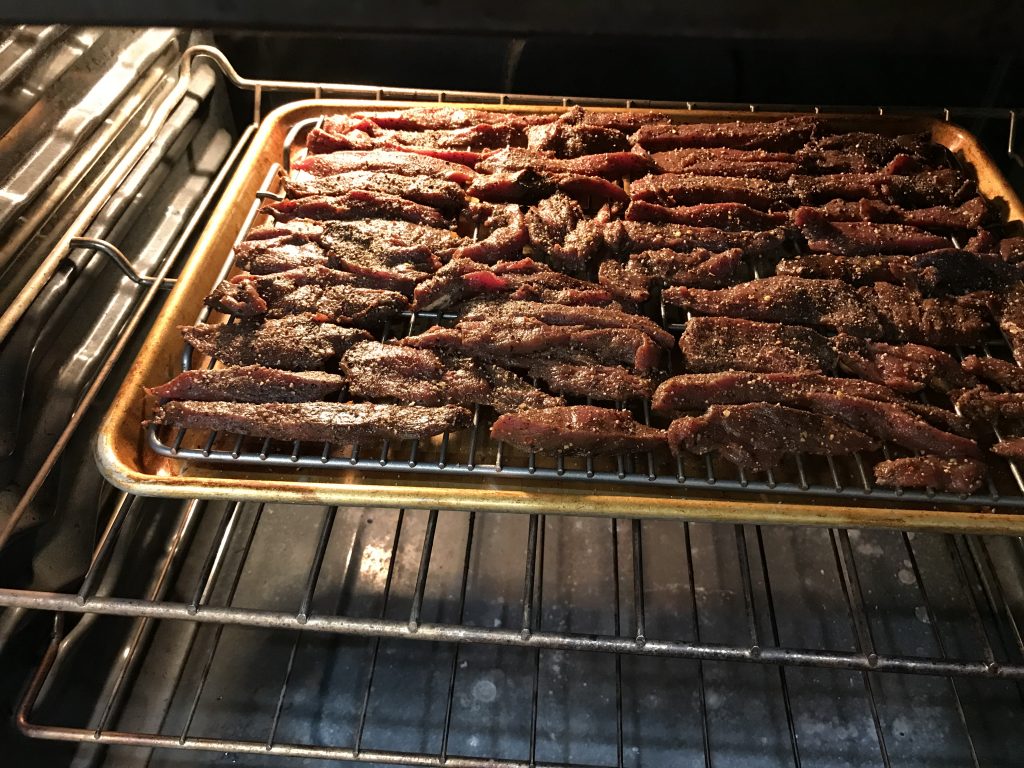 venison jerky pieces on cooling rack on cookie sheet in oven