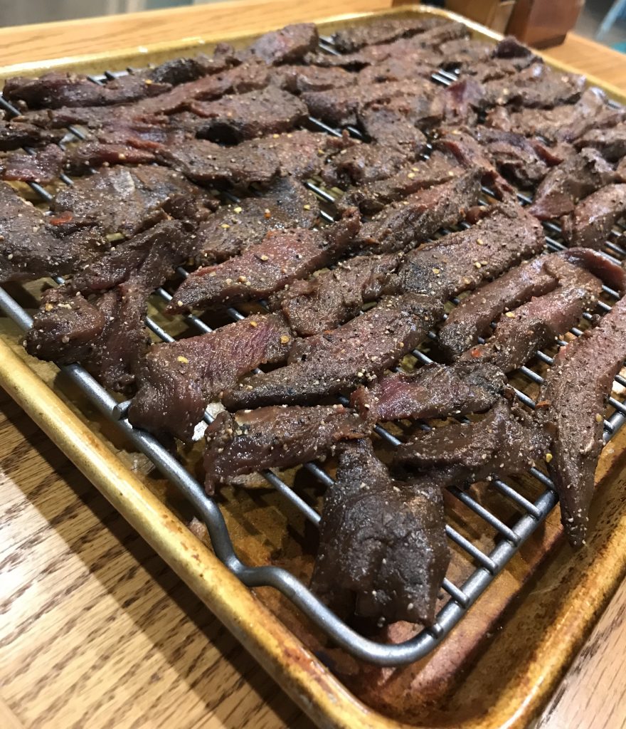 Venison meat jerky strips on rack on pan